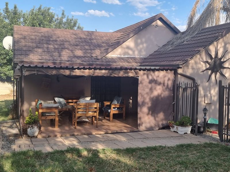 Rear view of the property featuring a covered patio area, tiled roof, and secure metal perimeter fencing set within a garden space.