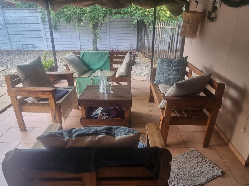 A covered outdoor patio area featuring tiled flooring, providing a functional space for relaxation overlooking the rear garden and boundary wall.