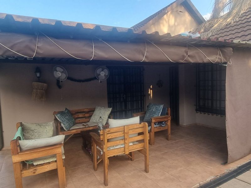A covered outdoor patio area featuring tiled flooring, wall-mounted fans, and security bars, providing a functional space for outdoor relaxation.