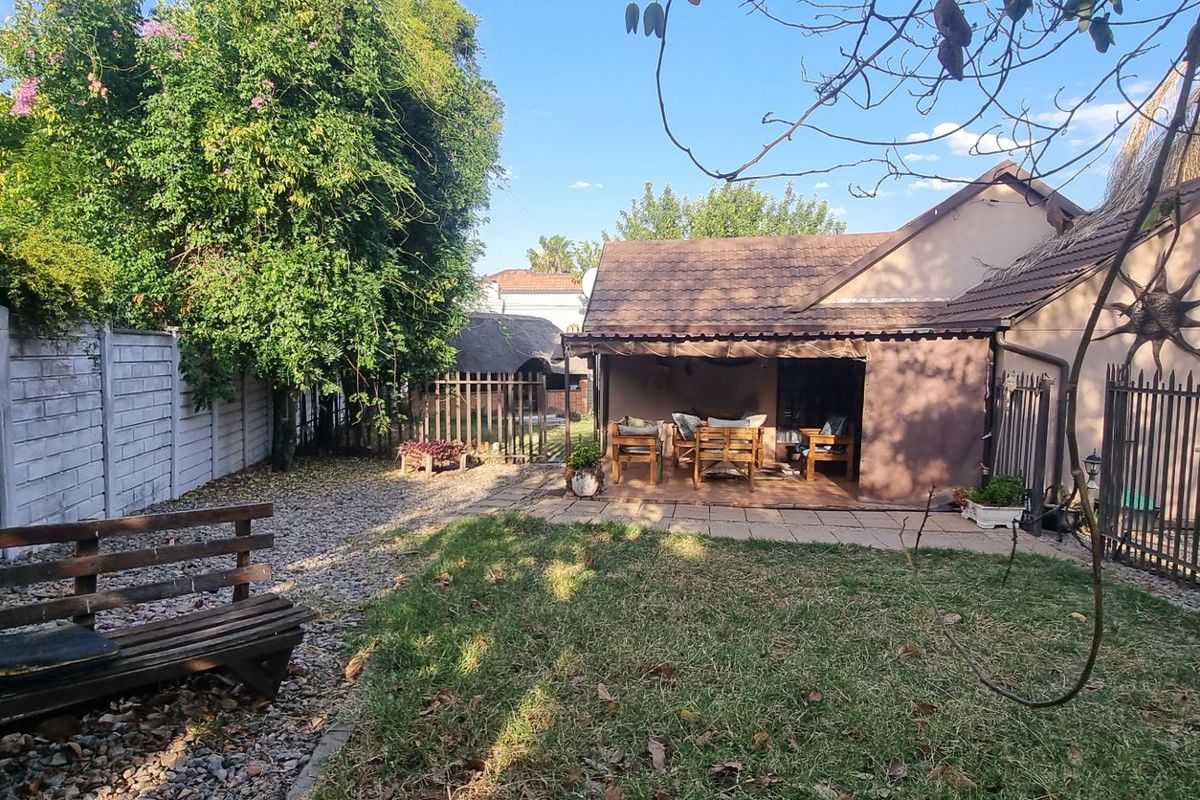 Rear view of the property featuring a covered patio, paved outdoor area, and a private garden enclosed by precast concrete and metal fencing.