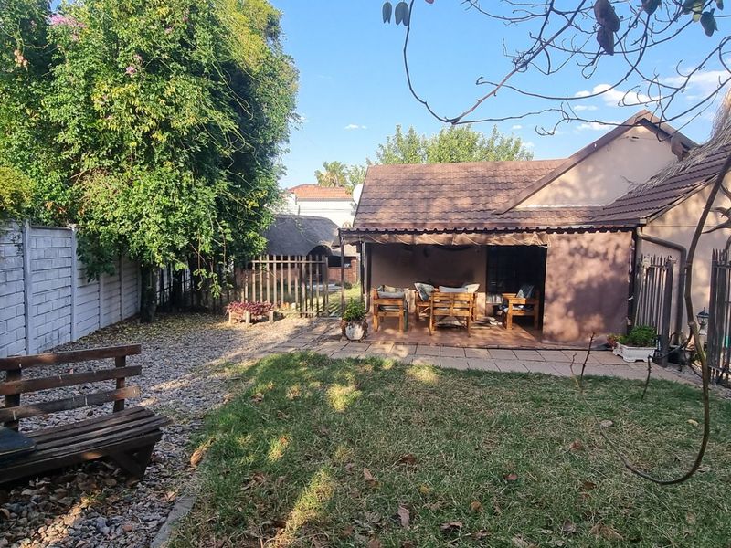Rear view of the property featuring a covered patio, paved outdoor area, and a private garden enclosed by precast concrete and metal fencing.