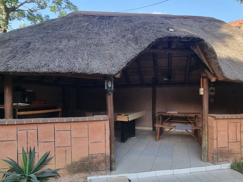 A rustic outdoor entertainment area featuring a traditional thatch roof, brick masonry walls, and tiled flooring, providing a covered space for outdoor gatherings.