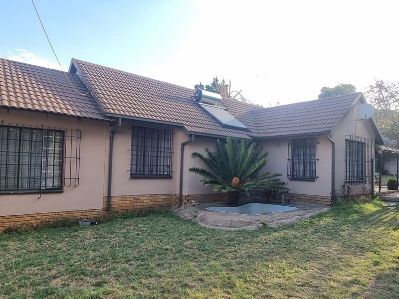 Rear view of the house featuring a tiled roof, solar water heating system, and security bars on windows, set against a garden area.
