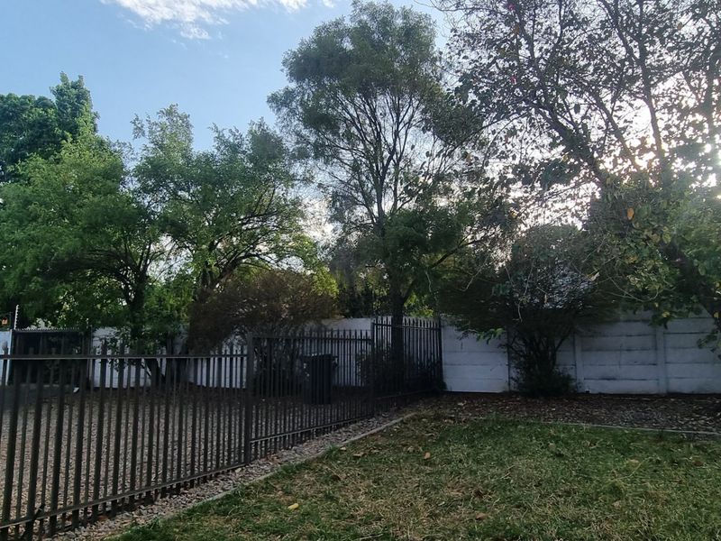 A private garden area featuring established trees, a grass lawn, and secure metal perimeter fencing with a precast concrete boundary wall.