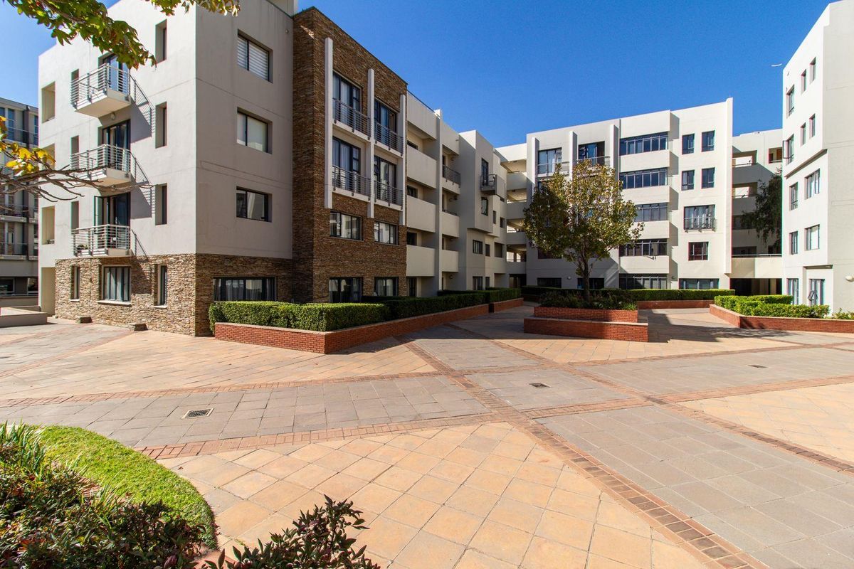 A well-maintained apartment complex courtyard featuring paved walkways, brick planter boxes, and modern building facades with stone accents and balconies.