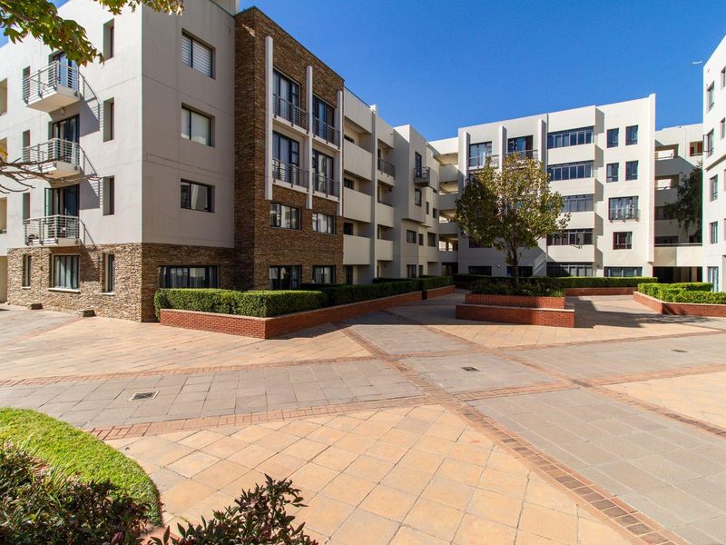 A well-maintained apartment complex courtyard featuring paved walkways, brick planter boxes, and modern building facades with stone accents and balconies.