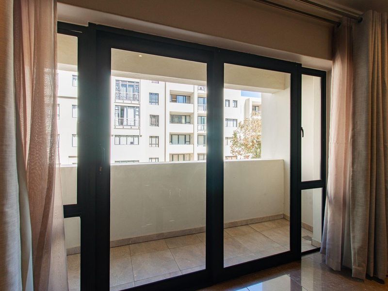 A view from an interior room looking out through a large sliding glass door onto a private balcony with tiled flooring.