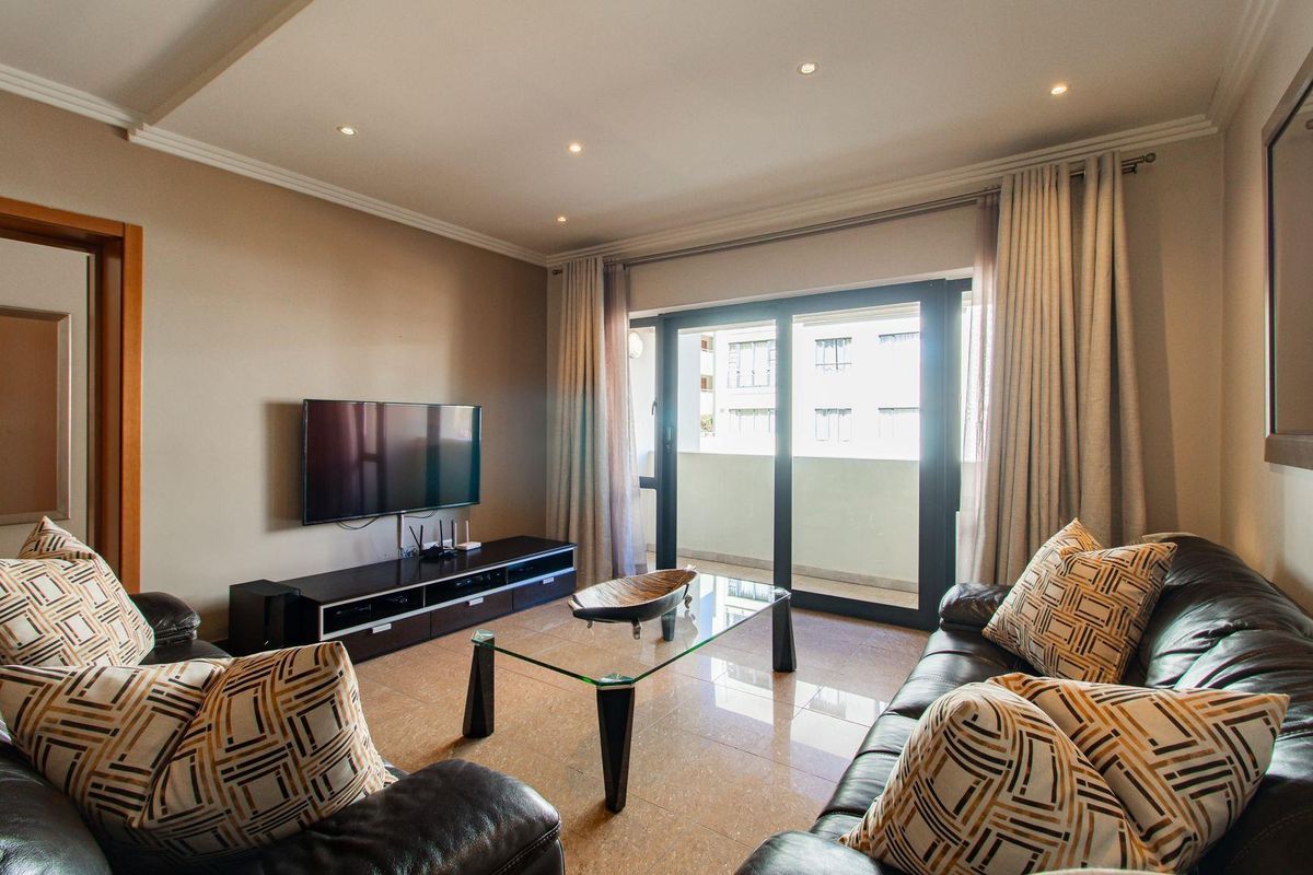 A well-maintained living room featuring tiled flooring, recessed ceiling lighting, and a sliding glass door providing access to a private balcony.