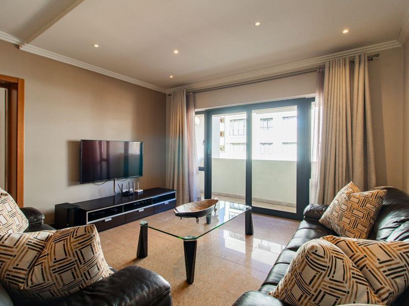 A well-maintained living room featuring tiled flooring, recessed ceiling lighting, and a sliding glass door providing access to a private balcony.