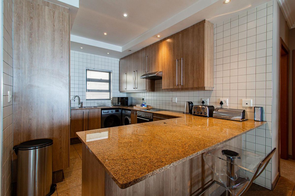 Modern kitchen featuring wood-finish cabinetry, granite countertops, integrated appliances, and a breakfast bar, complemented by tiled walls and recessed lighting.