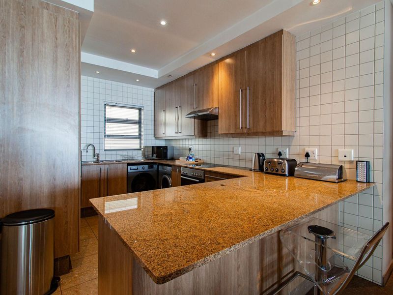 Modern kitchen featuring wood-finish cabinetry, granite countertops, integrated appliances, and a breakfast bar, complemented by tiled walls and recessed lighting.