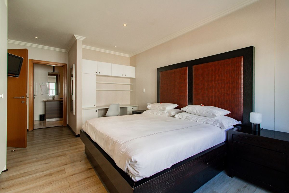 Spacious bedroom featuring built-in desk and cabinetry, laminate flooring, crown molding, and direct access to an en-suite bathroom.