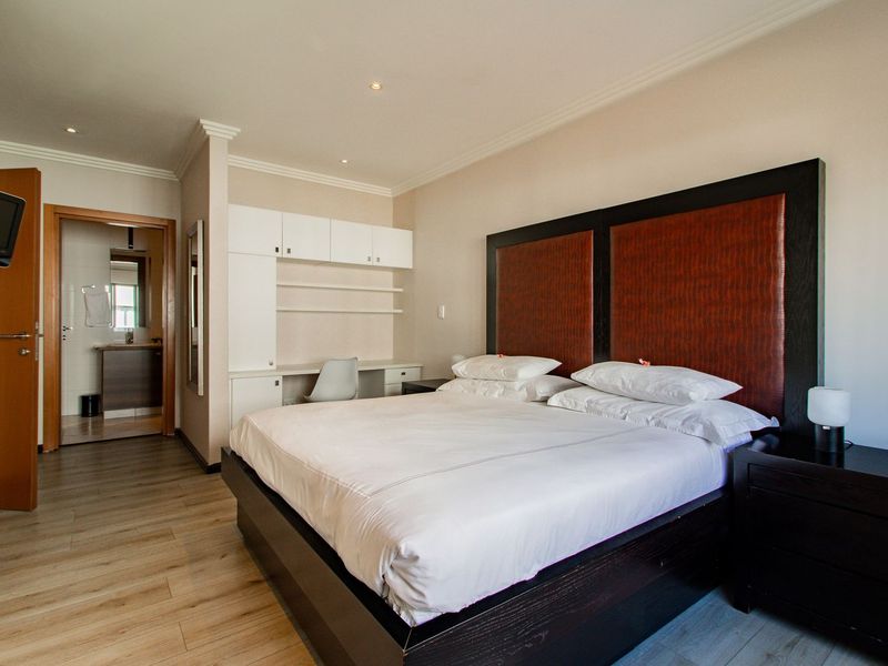Spacious bedroom featuring built-in desk and cabinetry, laminate flooring, crown molding, and direct access to an en-suite bathroom.