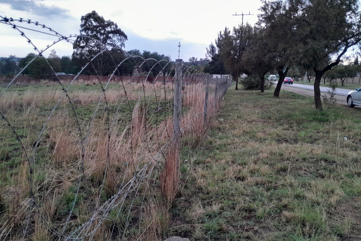 A view of the vacant residential land perimeter, featuring existing razor wire fencing and wooden posts along the roadside boundary.