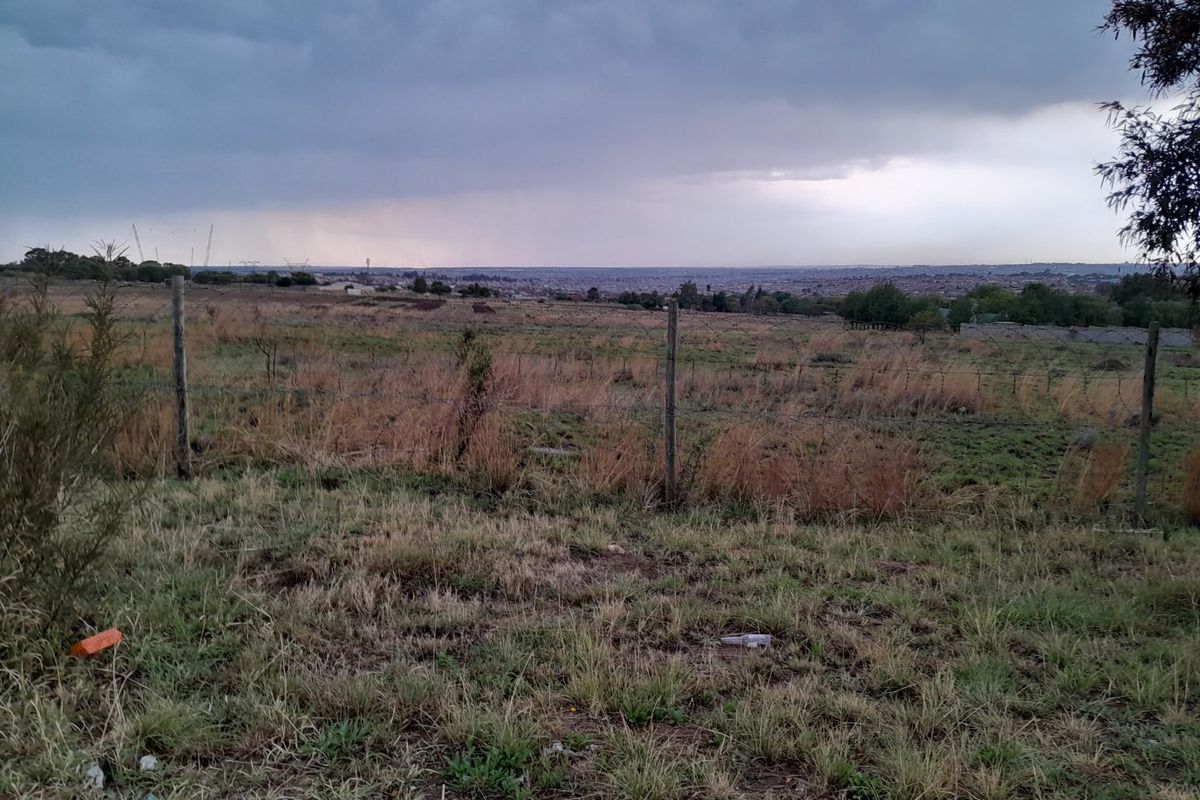 A wide-angle view of a vacant residential plot featuring natural grassland and perimeter wire fencing under an overcast sky.