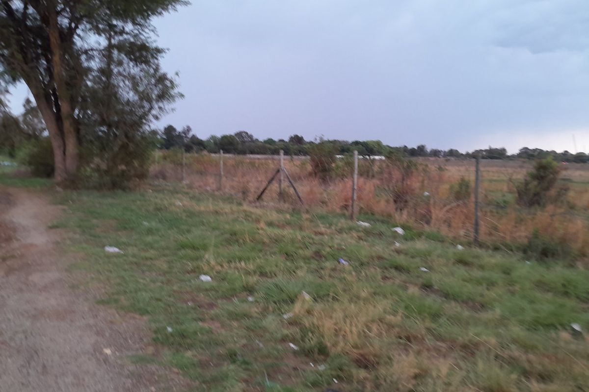 A view of a vacant residential plot featuring a wire fence boundary and natural vegetation.