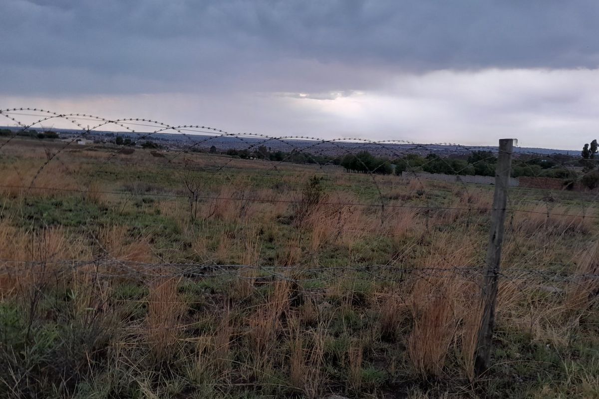 A view of a vacant residential plot featuring natural grass terrain and secured with barbed wire fencing.