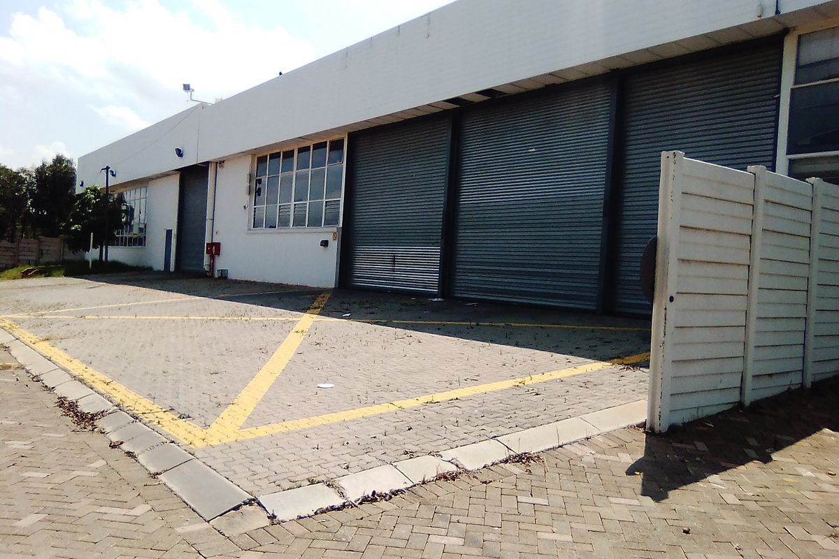 Commercial industrial property exterior featuring multiple roller shutter doors, paved parking area, and secure boundary walling.