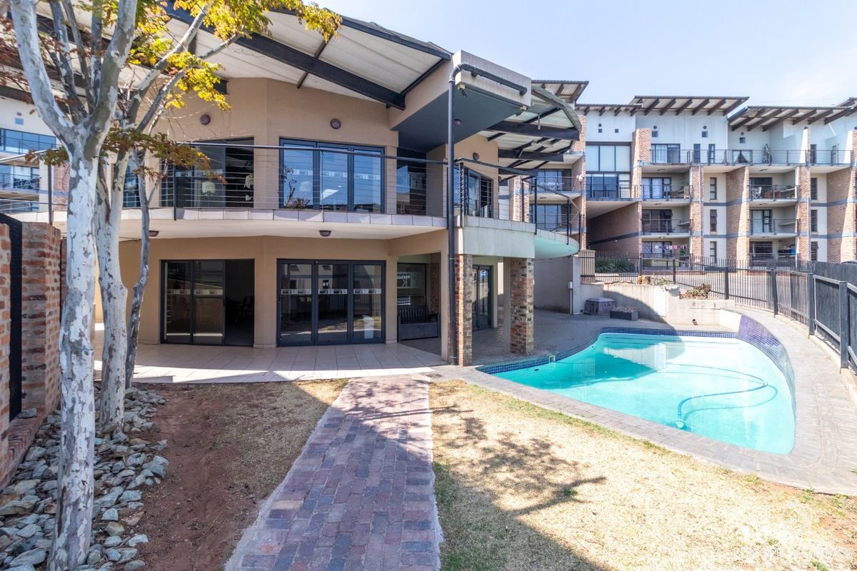 Rear view of the apartment complex featuring a swimming pool, tiled patio area, and upper-level balconies with modern architectural design.