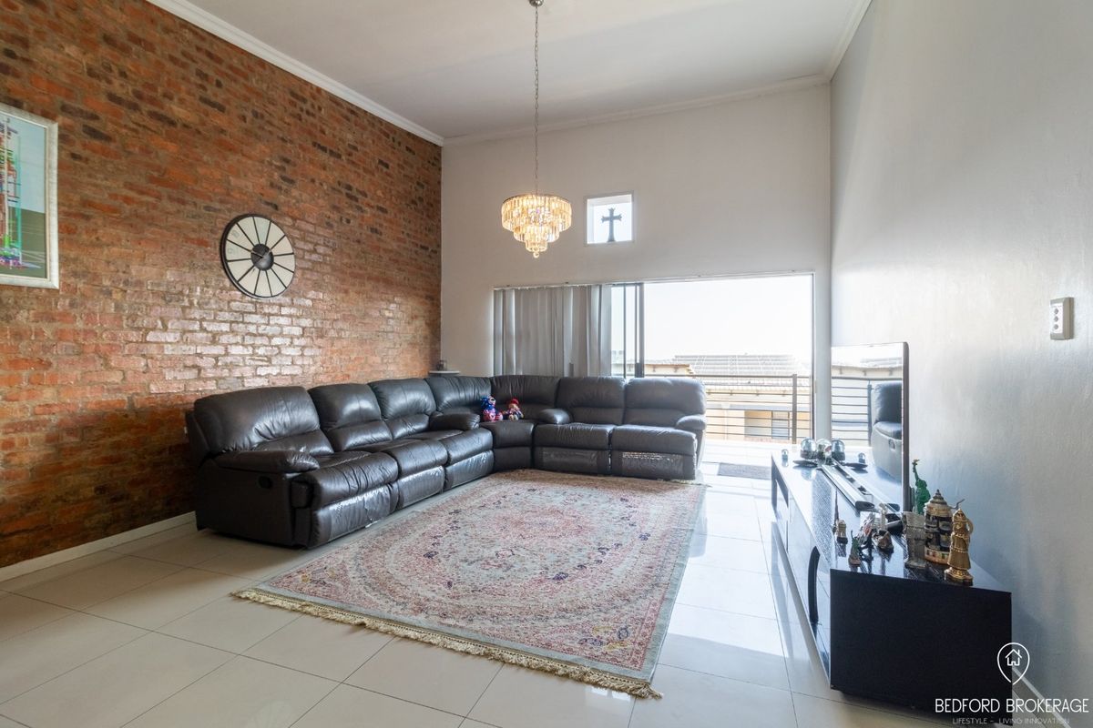 Spacious living room featuring an exposed brick wall, high ceilings with a chandelier, tiled floors, and direct access to a balcony through sliding doors.