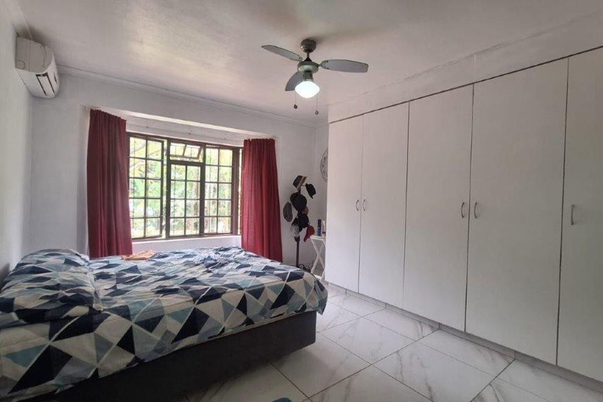 A spacious bedroom featuring large built-in cupboards, tiled flooring, a ceiling fan, and an air conditioning unit for climate control.