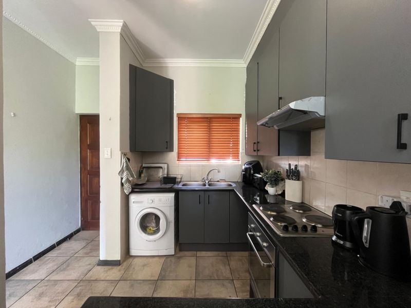 Modern kitchen featuring dark grey cabinetry, granite countertops, integrated oven and hob, and tiled flooring with a convenient laundry connection.