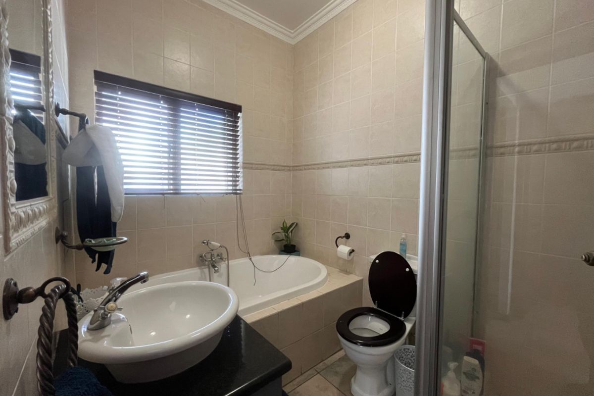 A functional bathroom featuring a built-in bathtub, separate shower enclosure, vanity basin, and toilet with neutral wall tiling and classic crown molding.