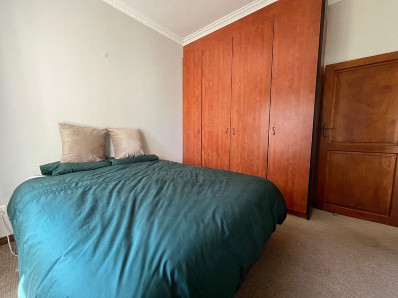 A bedroom featuring a large built-in wooden wardrobe, classic ceiling cornicing, and carpeted flooring, offering a functional and traditional layout.
