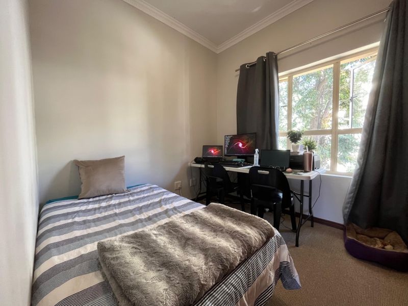 A functional bedroom featuring carpeted flooring, a large window allowing natural light, and decorative cornice detailing.