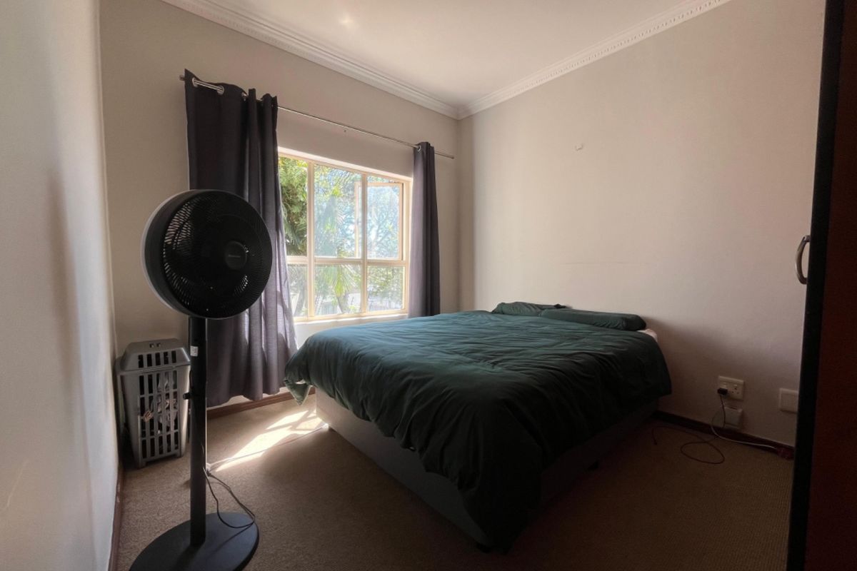 A simple bedroom featuring carpeted flooring, neutral walls, and a window with curtains, providing a functional and well-lit sleeping space.