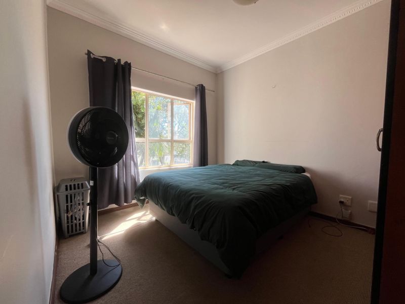 A simple bedroom featuring carpeted flooring, neutral walls, and a window with curtains, providing a functional and well-lit sleeping space.