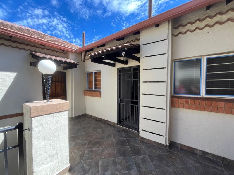 A well-maintained apartment entrance featuring tiled flooring, a secure metal gate, and protective window bars under a tiled roof.