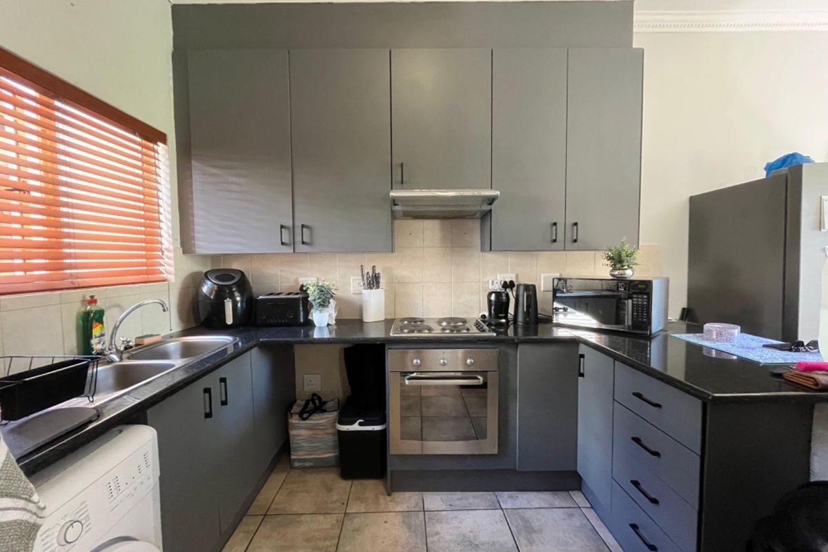 A functional kitchen featuring dark grey cabinetry, granite countertops, stainless steel appliances, and tiled flooring, offering a clean and practical workspace.