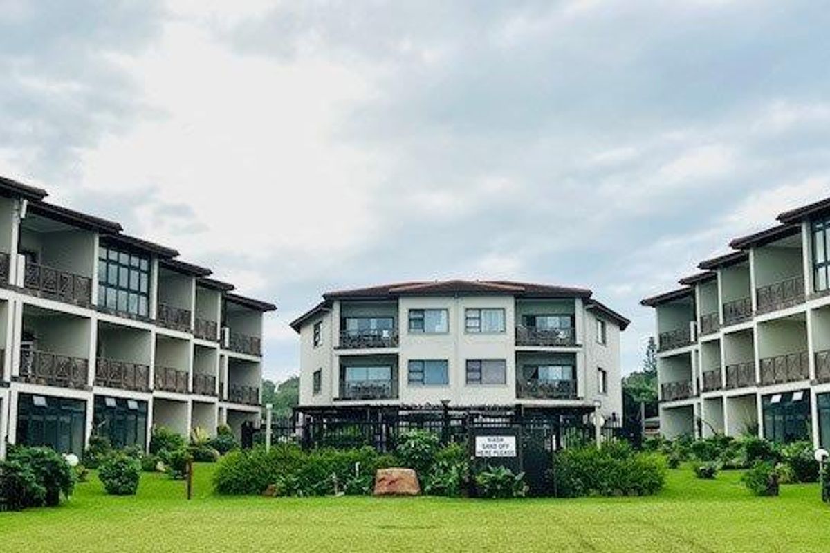 Exterior view of a multi-story apartment complex featuring landscaped gardens, balconies with decorative railings, and paved walkways between building blocks.