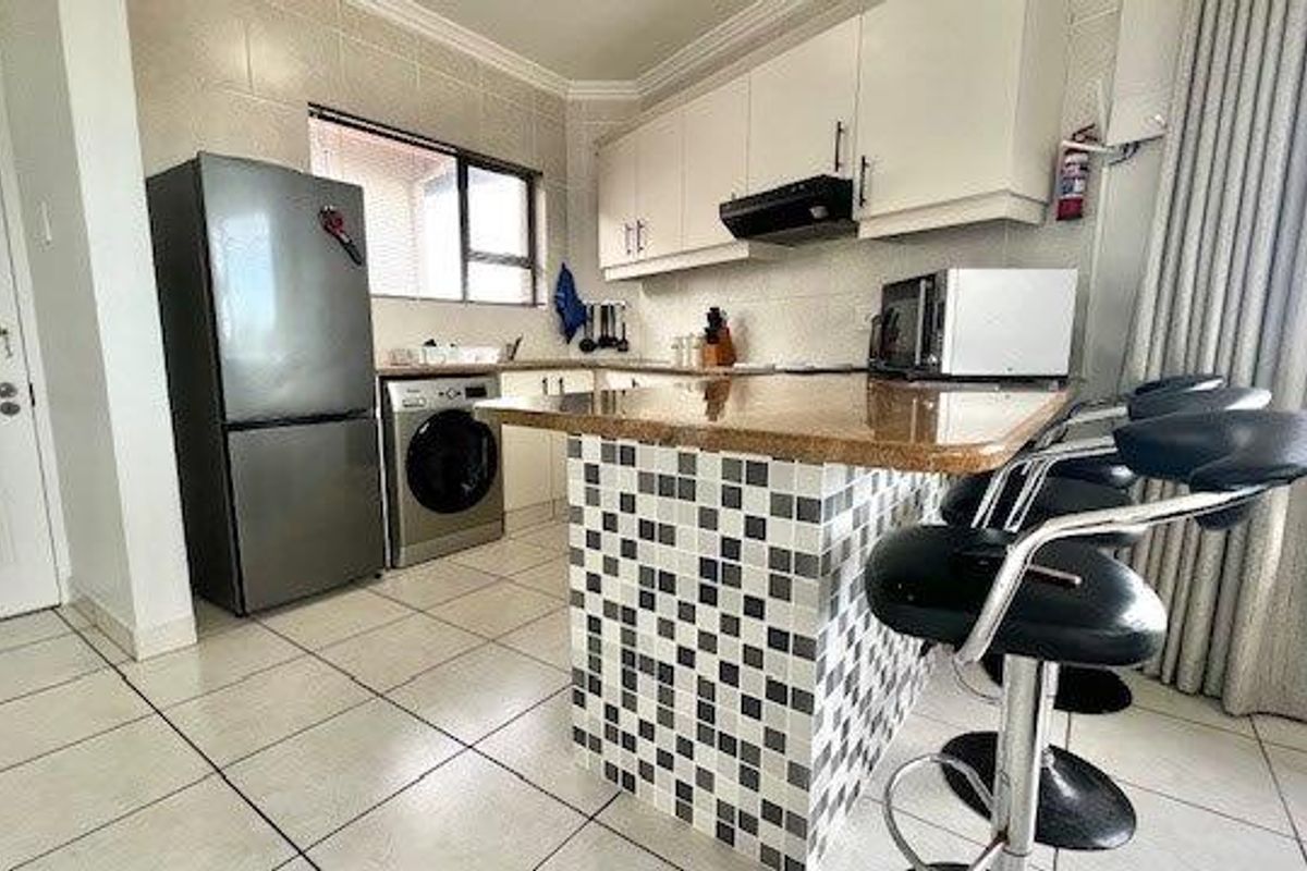 Compact kitchen featuring a breakfast bar with mosaic tiling, built-in cabinetry, tiled flooring, and integrated space for laundry appliances.