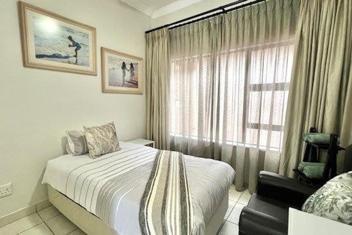 A well-lit bedroom featuring tiled flooring, large windows with floor-to-ceiling curtains, and neutral wall finishes.