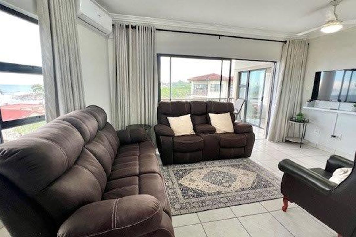 A bright living room featuring large windows with ocean views, tiled flooring, a ceiling fan, and a wall-mounted air conditioning unit.