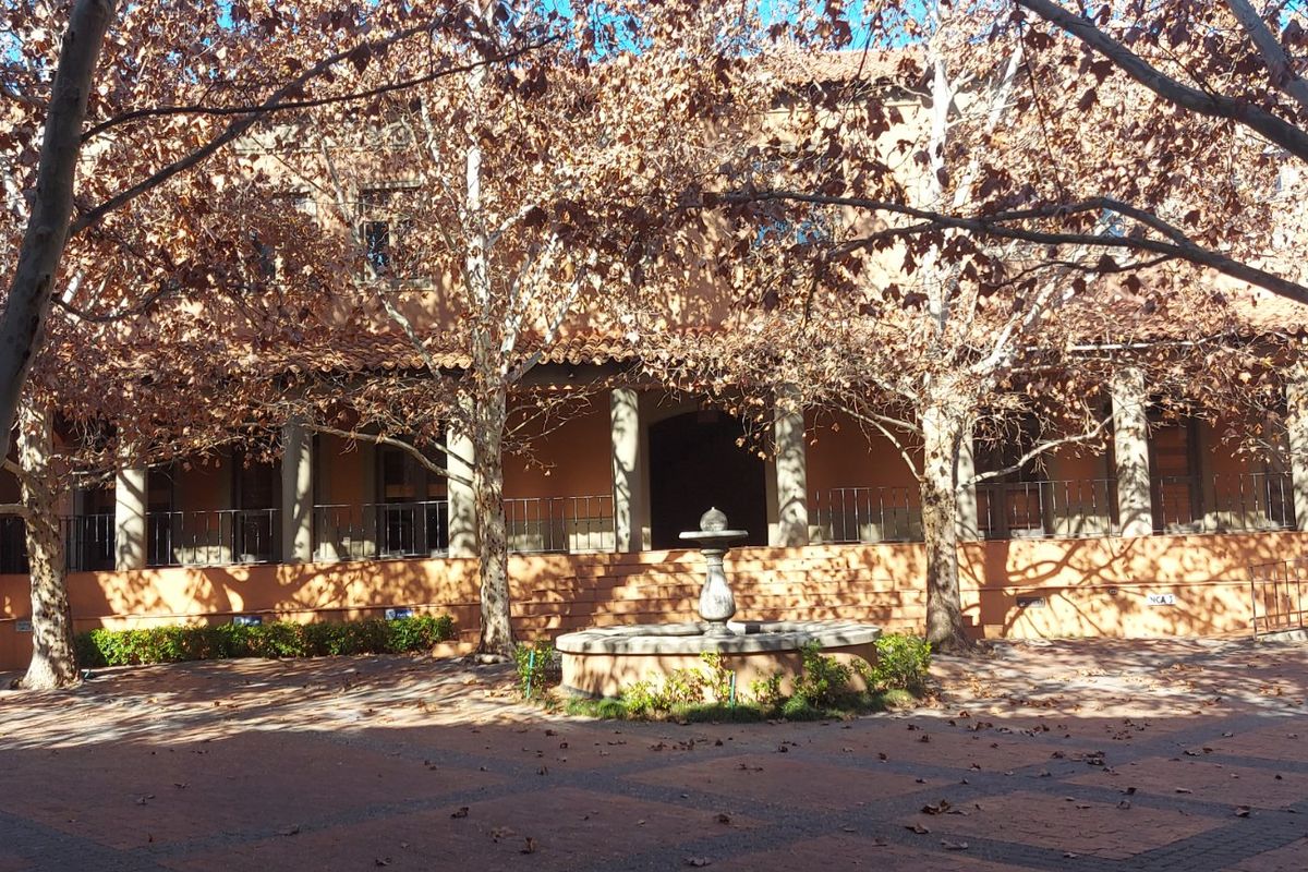 A spacious rear courtyard featuring a central stone fountain, paved flooring, and a covered veranda with stone columns and wrought iron railings.