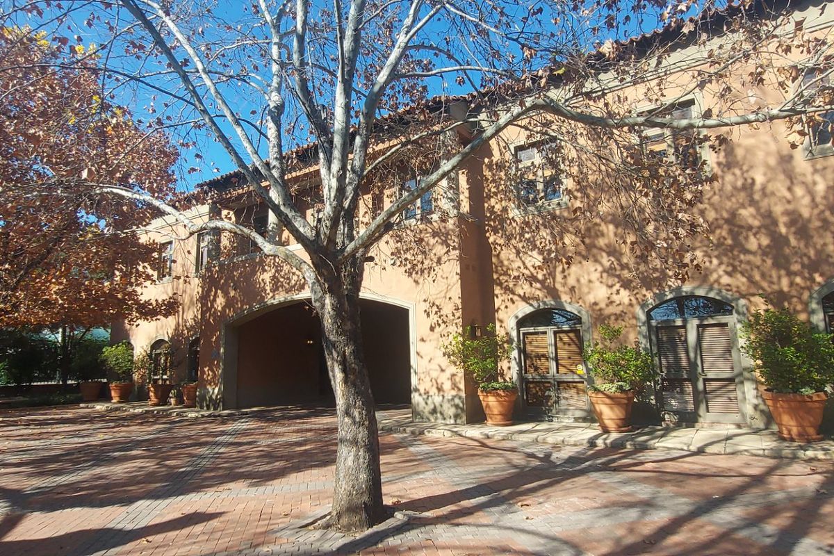 A well-maintained commercial building facade featuring stucco walls, arched windows, and a brick-paved entrance area with mature trees.