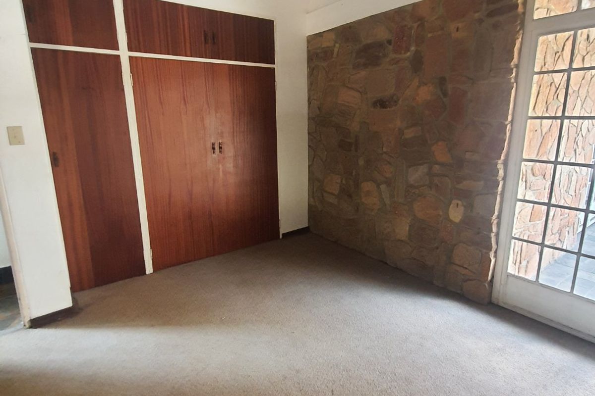 Empty bedroom featuring a rustic stone accent wall, built-in wooden cupboards, and a high thatched ceiling with direct access to the exterior.