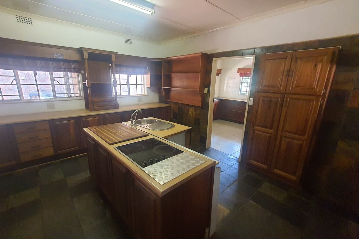 Spacious kitchen featuring wooden cabinetry, a central island with an integrated cooktop, double sink, and durable slate tile flooring throughout.