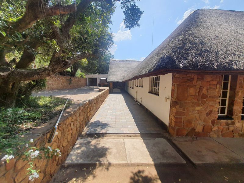 A view of the rear exterior featuring a traditional thatched roof, stone-clad walls, and a paved walkway leading towards a detached garage.