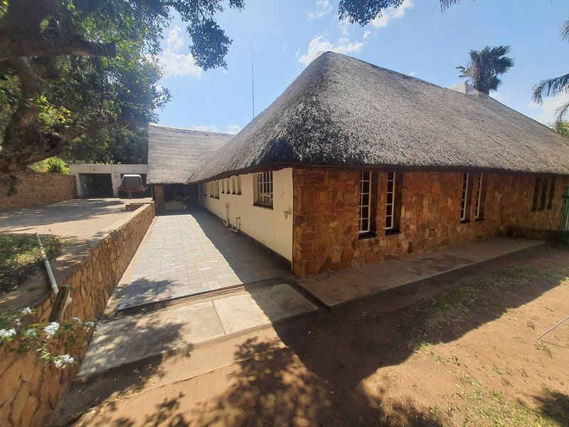 Rear view of a farm-style residence featuring traditional thatch roofing, stone exterior cladding, and a paved walkway leading to the main structure.