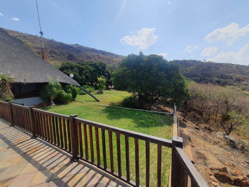 Elevated timber-railed patio overlooking a lush garden and natural landscape, featuring traditional thatched roof architecture.