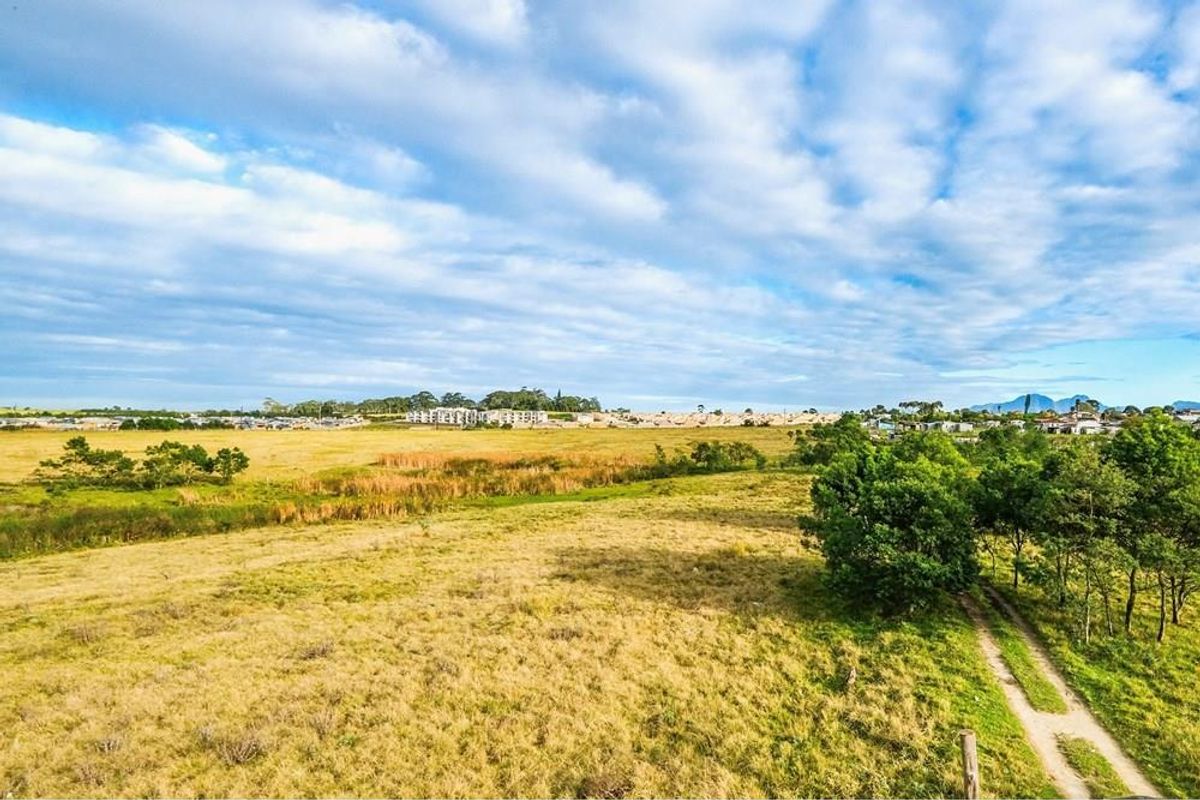An aerial view of a large, open vacant residential plot featuring natural grassland, scattered trees, and a dirt access track.