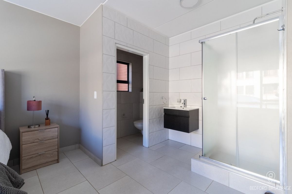 Modern en-suite bathroom featuring a glass shower enclosure, wall-mounted vanity, and neutral tiling, with an adjoining private toilet area.