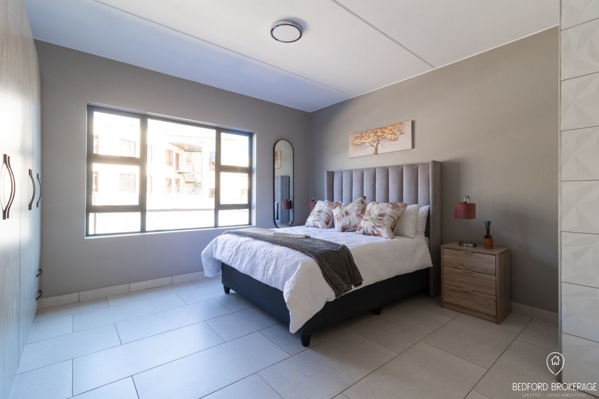 A well-maintained bedroom featuring neutral wall tones, large windows for natural light, tiled flooring, and ample built-in cupboard storage.