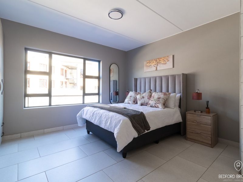 A well-maintained bedroom featuring neutral wall tones, large windows for natural light, tiled flooring, and ample built-in cupboard storage.