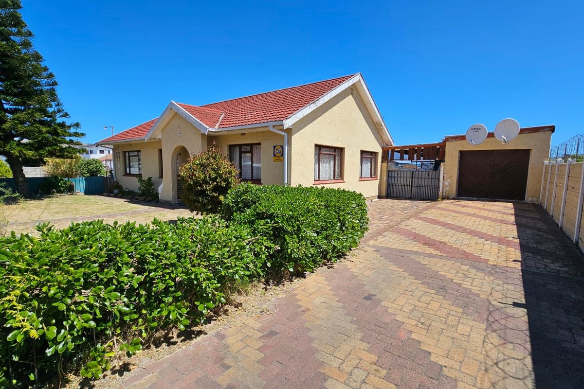 Front view of a residential property featuring a tiled roof, paved driveway, attached garage, and secure boundary walling.