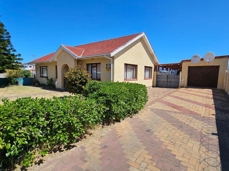 Front view of a residential property featuring a tiled roof, paved driveway, attached garage, and secure boundary walling.